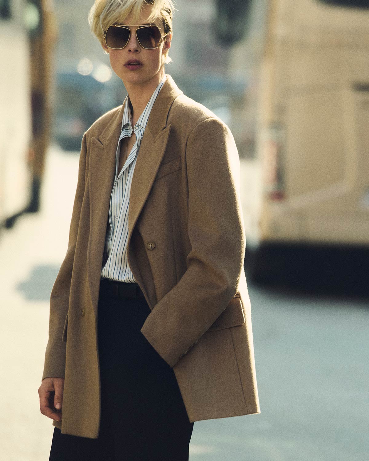 Model in double-breasted blazer-style Max Mara Olimpia Jacket in camel colour, with dark glasses and shirt in an urban environment.